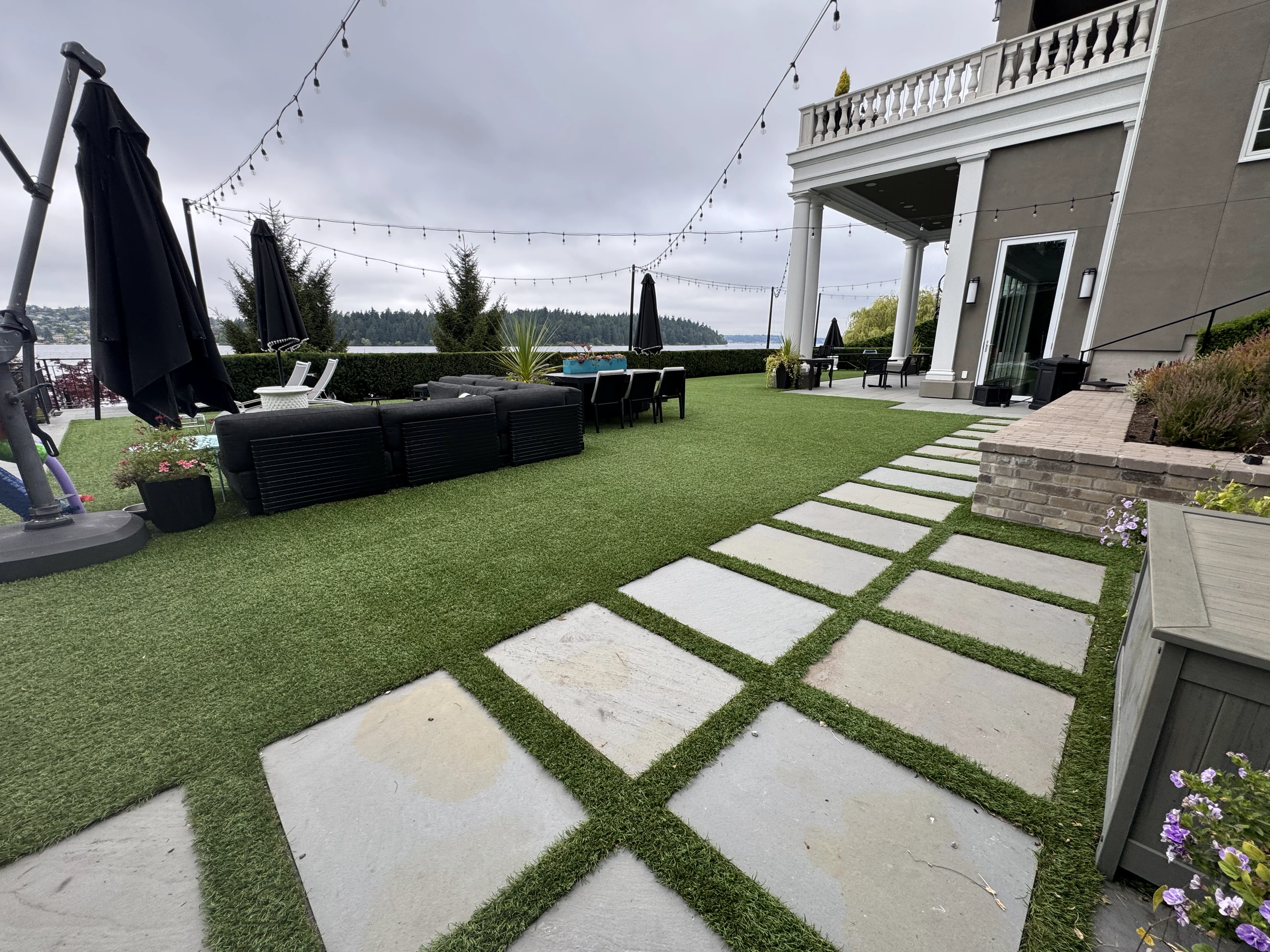Turf surrounding stone pavers and outdoor seating overlooking the water